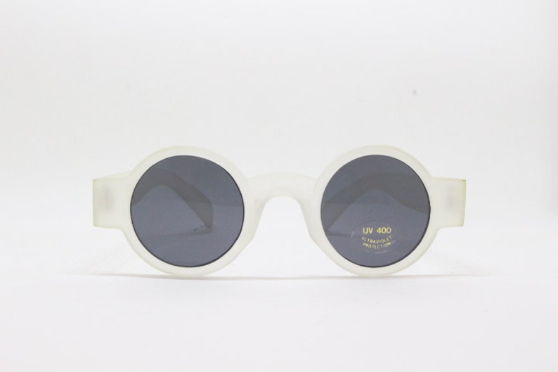 May include: White round sunglasses with dark gray lenses. The sunglasses have UV 400 ultraviolet protection printed on the right lens.