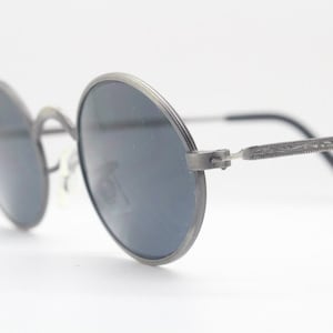 Occhiali da sole ovali vintage anni '90. Montatura in metallo dal design anni '20 con finitura satinata spazzolata, lenti nere e aste fantasia. NO. Steampunk vittoriano