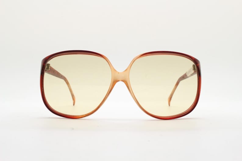 Op de afbeelding: Oversized vintage zonnebril met een bruin schildpadmontuur en geel getinte glazen. De bril heeft een grote, afgeronde vorm, met een brug die de twee glazen verbindt. De pootjes zijn dun en lopen door naar de oren.