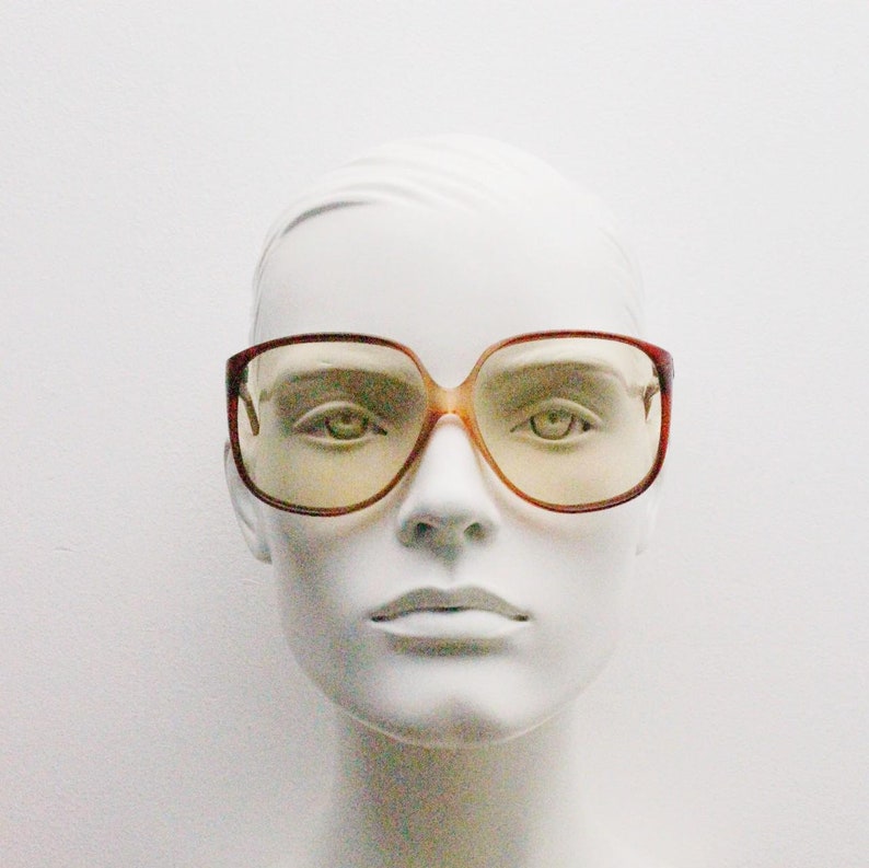 Op de afbeelding: Oversized bril in vintage-stijl met een bruin montuur en geel getinte glazen. De bril heeft een vierkante vorm en wordt getoond op een witte mannequinhoofd. Een retro accessoire.