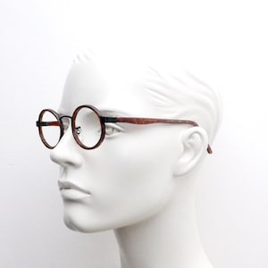 May include: A pair of round, brown tortoiseshell spectacles with black metal accents. The glasses are on a white mannequin head.