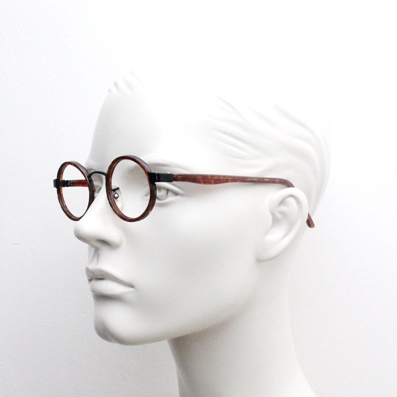 May include: A pair of round, brown tortoiseshell spectacles with black metal accents. The glasses are on a white mannequin head.