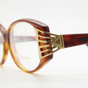 May include: Brown tortoiseshell eyeglasses with gold metal accents on the temples. The glasses have a vintage style and are in good condition.