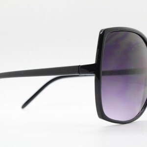Puede incluir: Gafas de sol cuadradas negras con un marco negro grueso y lentes de color p&uacute;rpura oscuro.