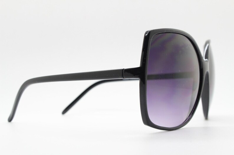 Puede incluir: Gafas de sol cuadradas negras con un marco negro grueso y lentes de color p&uacute;rpura oscuro.