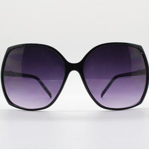 Puede incluir: Gafas de sol negras de gran tama&ntilde;o con montura cuadrada y lentes de color morado oscuro.