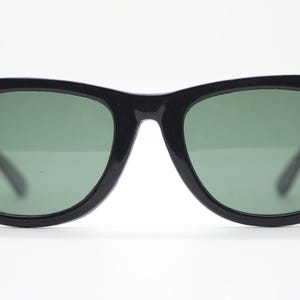 Puede incluir: Gafas de sol negras con un dise&ntilde;o cl&aacute;sico. Las monturas son de color negro brillante y las lentes son de un verde apagado. Las gafas de sol tienen forma rectangular con una ligera curva en la parte superior. Las patillas son finas y negras.