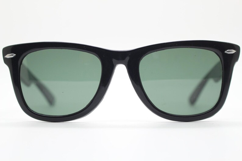 Puede incluir: Gafas de sol negras con un dise&ntilde;o cl&aacute;sico. Las monturas son de color negro brillante y las lentes son de un verde apagado. Las gafas de sol tienen forma rectangular con una ligera curva en la parte superior. Las patillas son finas y negras.