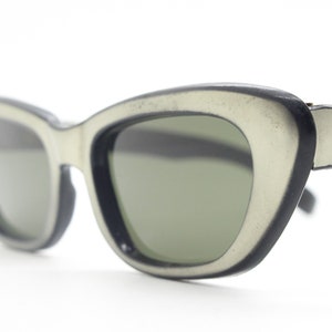 Może przedstawiać: Czarno-białe okulary przeciwsłoneczne typu "kocie oko" z zielonymi szkłami.