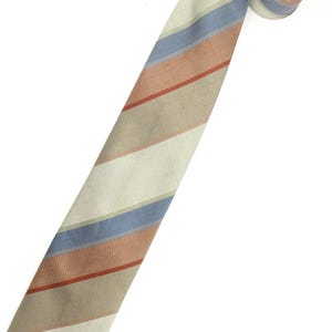 Op de afbeelding: Een gestreepte stropdas in beige, blauwe en roesttinten. De stropdas heeft een opgerold uiteinde. De kleuren zijn gedempt, wat een klassieke en veelzijdige uitstraling geeft. De stropdas is waarschijnlijk gemaakt van een geweven stof.
