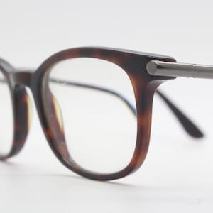 Może przedstawiać: Okulary w kolorze żółwim z metalowymi srebrnymi akcentami na zausznikach.