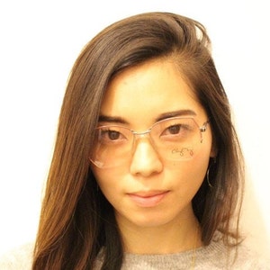 Könnte beinhalten: Eine Frau mit langen braunen Haaren trägt eine silberne Brille mit rosa Tönung. Die Brille hat den Text "Chloe" auf der rechten Linse.