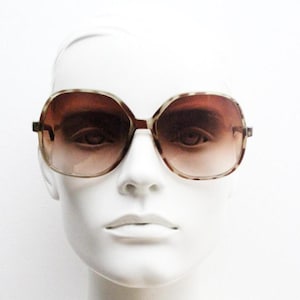May include: Large brown sunglasses with a tortoiseshell pattern on the frames and gradient lenses. The sunglasses have a square shape and are displayed on a white mannequin head. The lenses transition from a darker shade at the top to a lighter shade at the bottom.