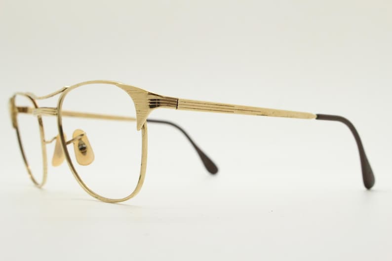 Puede incluir: Gafas de metal dorado con patillas de pl&aacute;stico marr&oacute;n. Las gafas tienen una forma rectangular redondeada.