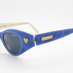 Op de afbeelding: Blauwe en witte zonnebril met een hartvormig detail op het montuur. De zonnebril heeft een gouden logo met de tekst "Emilio Pucci".