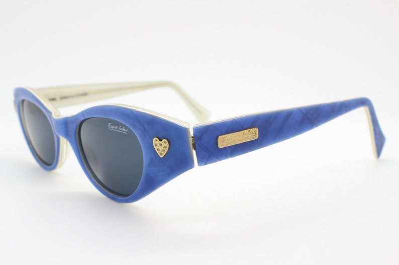 Op de afbeelding: Blauwe en witte zonnebril met een hartvormig detail op het montuur. De zonnebril heeft een gouden logo met de tekst "Emilio Pucci".