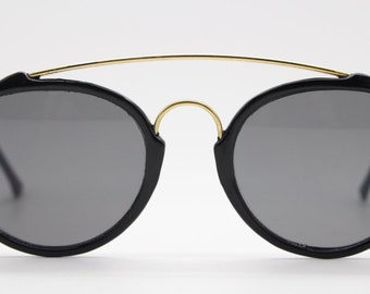 Gafas de sol vintage estilizadas de los 90. Gafas negras redondas de doble puente con barra de cejas dorada arqueada. NOS sin usar.