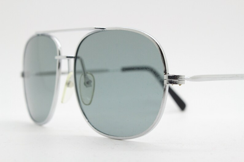 May include: Silver aviator sunglasses with gray lenses. The sunglasses have a metal frame and are in focus.