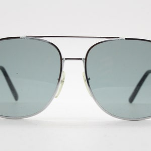 May include: Silver aviator sunglasses with gray lenses. The sunglasses have a classic design with a thin metal frame.
