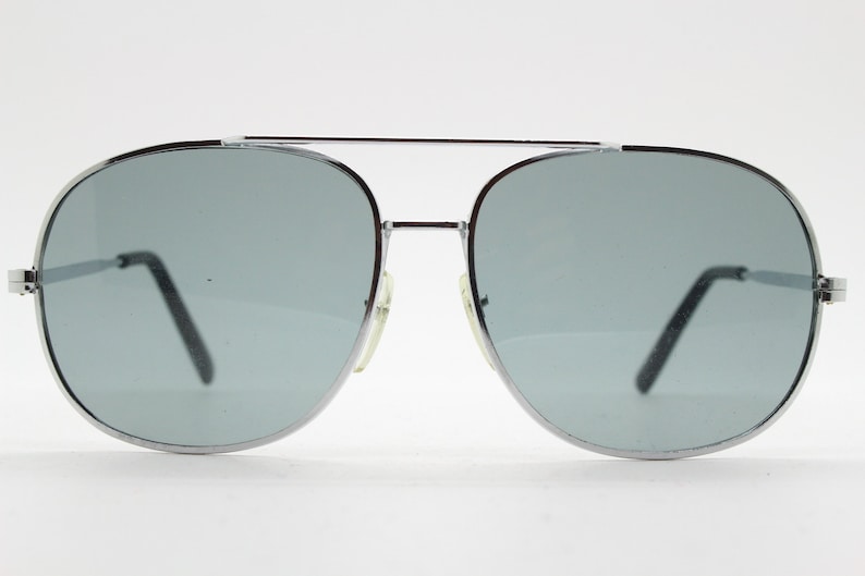 May include: Silver aviator sunglasses with gray lenses. The sunglasses have a classic design with a thin metal frame.