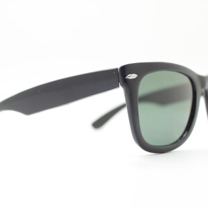 Puede incluir: Gafas de sol negras con un dise&ntilde;o cl&aacute;sico y retro. Las monturas son gruesas y angulares, con un acabado brillante. Las lentes son de color verde oscuro, contrastando con las monturas negras. Un accesorio elegante para la protecci&oacute;n ocular.