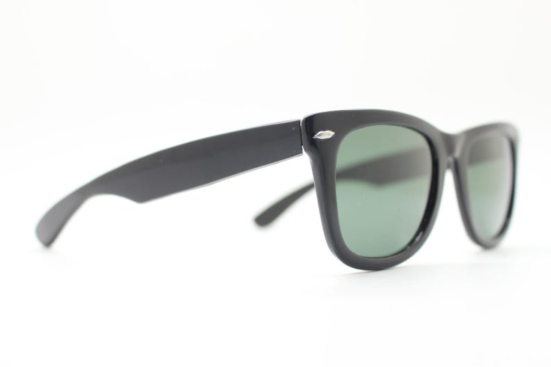 Puede incluir: Gafas de sol negras con un dise&ntilde;o cl&aacute;sico y retro. Las monturas son gruesas y angulares, con un acabado brillante. Las lentes son de color verde oscuro, contrastando con las monturas negras. Un accesorio elegante para la protecci&oacute;n ocular.