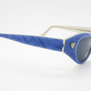 Op de afbeelding: Blauwe cat-eye zonnebril met een wit montuur en een klein hartvormig detail aan de zijkant.