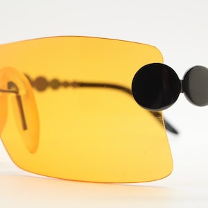May include: Orange tinted sunglasses with a black frame and round black accents on the arms.