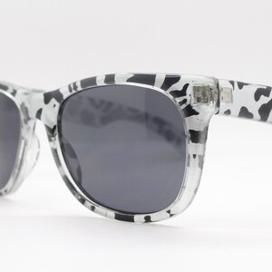 May include: Black and white patterned sunglasses with dark lenses. The sunglasses have a classic, rectangular shape.