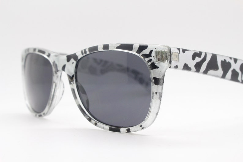 May include: Black and white patterned sunglasses with dark lenses. The sunglasses have a classic, rectangular shape.