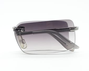 Puede incluir: Un par de gafas de sol con montura plateada y lentes grises degradados. Las gafas tienen una forma rectangular moderna.
