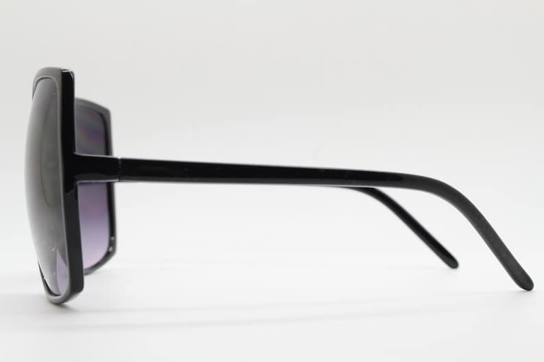 Puede incluir: Gafas de sol negras de gran tama&ntilde;o con montura cuadrada y patillas finas.