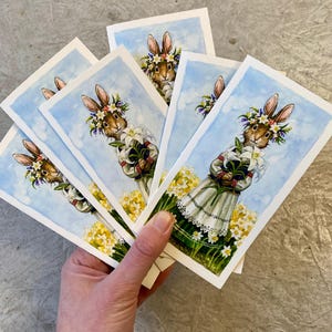 May include: A set of three ceramic mugs with a speckled, cream-colored glaze. Each mug features a different hand-painted floral design in shades of blue, green, and yellow. The mugs have a simple, rounded shape and a comfortable handle.