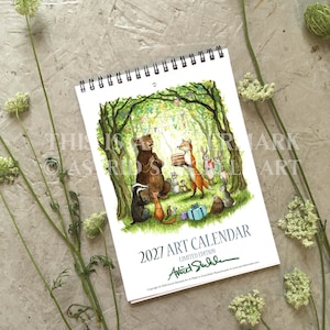 Może przedstawiać: Kalendarz artystyczny na rok 2027 ze spiralą, zawierający akwarelową ilustrację niedźwiedzia, lisa i innych zwierząt leśnych świętujących z tortem i prezentami. Tekst głosi 2027 ART CALENDAR LIMITED EDITION.