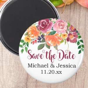 May include: A round white magnet with a floral design in shades of pink, orange, and burgundy. The text "Save the Date" is written in burgundy script, followed by "Michael & Jessica" and "11.20.XX".