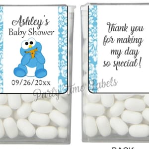 May include: A blue and white favor box filled with white mints. The front of the box has a label with a blue and white damask pattern and a cartoon cookie monster holding a cookie. The label says "Ashley's Baby Shower" and "09/26/20xx". The back of the box has a label with a blue and white damask pattern and the text "Thank you for making my day so special!"