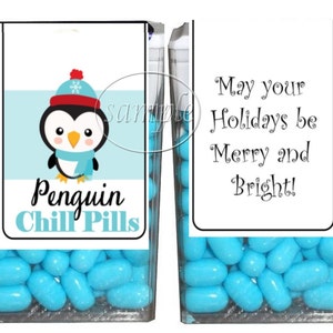 May include: Two clear plastic containers filled with blue candies. The container on the left has a label that says "Penguin Chill Pills" and features a cartoon penguin wearing a red and white hat. The container on the right has a label that says "May your Holidays be Merry and Bright!"