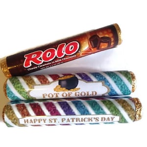 May include: Three wrapped chocolate candy bars. The top bar is a Rolo candy bar with the text "Chewy Caramels in Milk Chocolate". The middle bar has a rainbow striped wrapper with the text "Pot of Gold". The bottom bar has a rainbow striped wrapper with the text "Happy St. Patrick's Day".