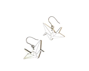 May include: A pair of silver earrings featuring origami crane designs. The cranes are made of metal and have a white finish.