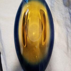 May include: A blue and amber glass bowl with a rounded oval shape. The bowl has a smooth, glossy finish.