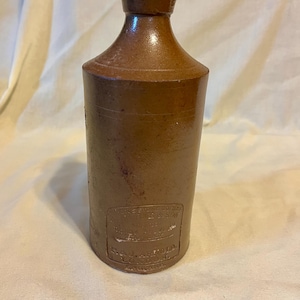 May include: A brown stoneware bottle with a cylindrical body and a narrow neck. The bottle features a rectangular embossed label near the base with the text P. & J. ARNOLD LONDON ENGLAND and other partially visible lettering.