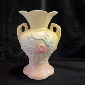 May include: A pale yellow and pink ceramic vase with a floral design. The vase has two handles and a scalloped rim.