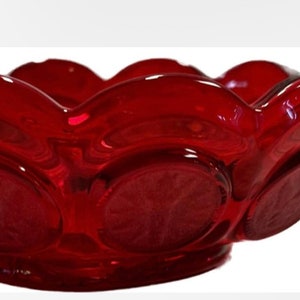 May include: A red glass dish with a scalloped edge and a single handle. The dish has a textured surface with a repeating pattern of circles.