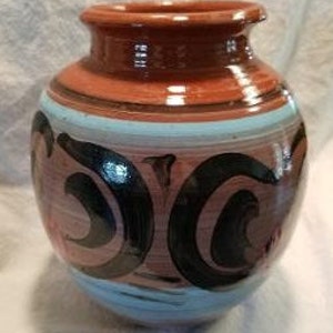 May include: A brown ceramic vase with blue and black painted designs. The vase has a rounded body and a wide mouth.