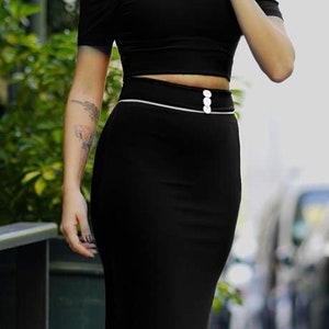 Puede incluir: Una falda midi negra con ribete blanco y tres botones blancos en la cintura.