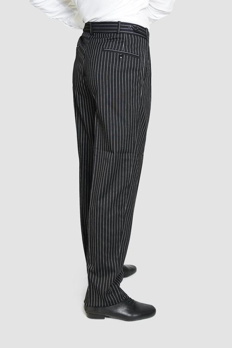 May include: Black pinstripe pants with a white stripe. The pants have a belt loop and a back pocket. The pants are worn with black shoes.