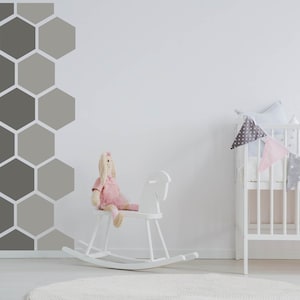 May include: A child's nursery with a white cot decorated with a star and polka dot bunting. A white rocking horse and a stuffed bunny in a pink dress are in the foreground. The wall has a geometric design of grey and light grey hexagons.