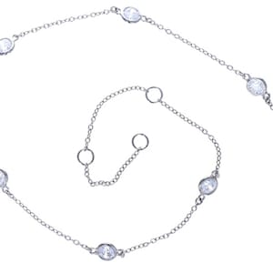 May include: A silver-toned necklace with seven clear, oval-shaped gemstones evenly spaced along a delicate chain. The necklace has a lobster clasp closure and adjustable chain length. The gemstones are set in a bezel setting.