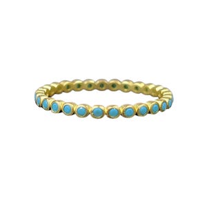 May include: A gold-colored ring with a series of small, round, turquoise-colored stones set around the band. The ring is set against a white background, highlighting the contrast between the gold and turquoise.
