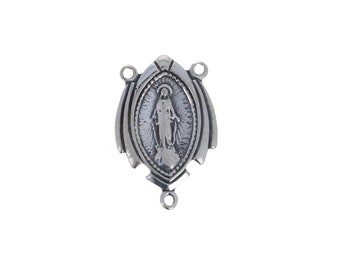 May include: A silver-toned rosary center with an oval-shaped centerpiece. The centerpiece features an engraved image of a religious figure with the words "AVE MARIA GRATIA PLENA" around the border. The piece has three holes for attachment.
